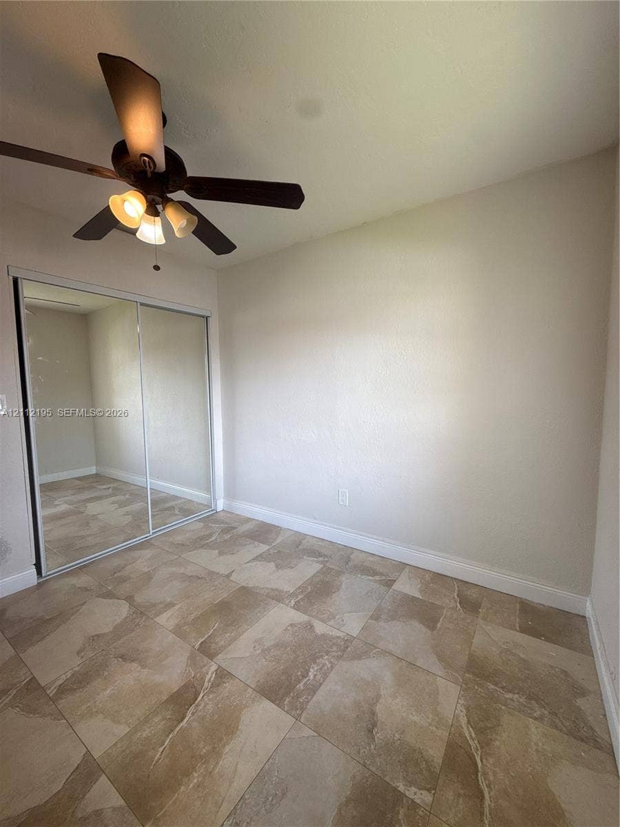11745 SW 122nd Place, #11745, Miami, Miami, FL 33186 Room featuring large-format tile flooring, mirrored sliding closet doors, and a ceiling-mounted light fixture with a multi-blade fan
