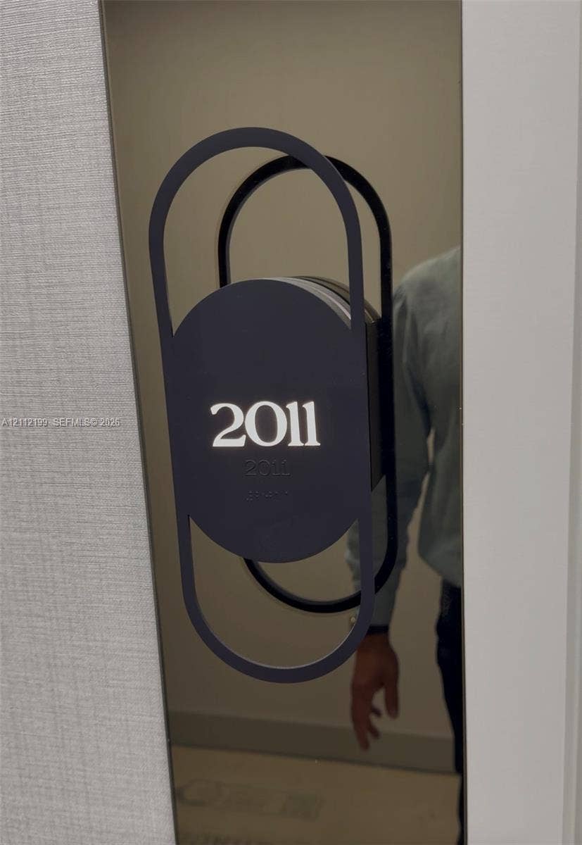 Modern metallic door plaque featuring a matte black geometric frame and integrated Braille signage