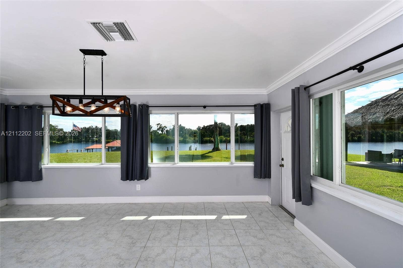 3233 Shell Lane, Labelle, FL 33935 Large windows with water frontage, rectangular tile flooring, crown molding, and a metal and glass geometric chandelier