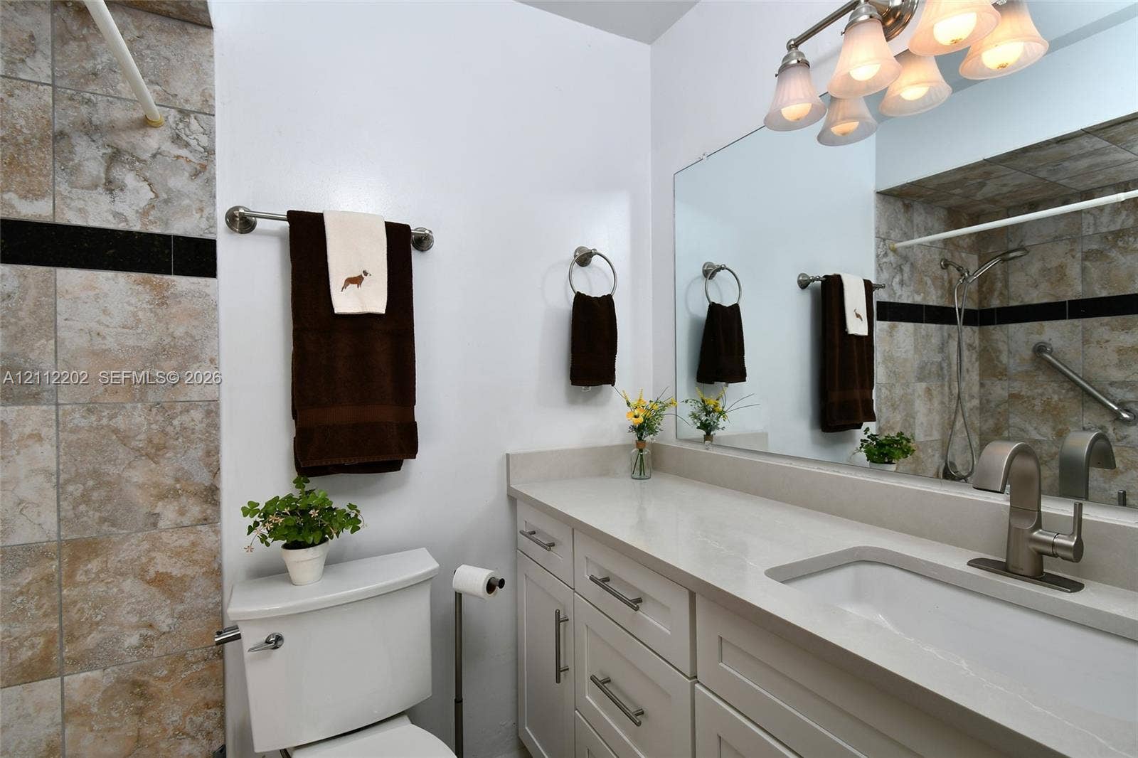 3233 Shell Lane, Labelle, FL 33935 Bathroom vanity featuring a light-toned solid surface countertop, an integrated rectangular sink, brushed nickel hardware, and multi-drawer cabinetry, complemented by stone-tiled shower surround with decorative black accent tile