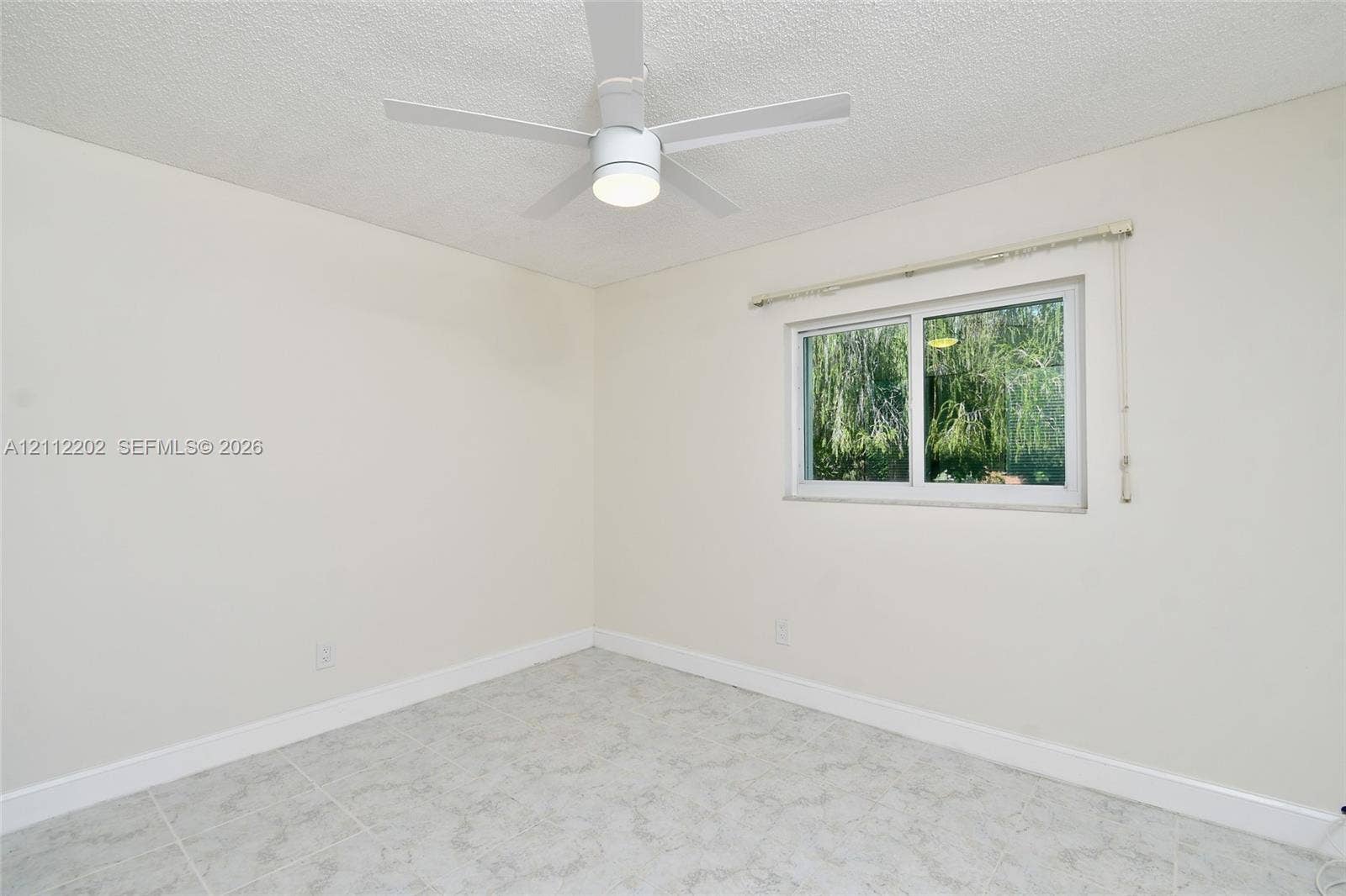 3233 Shell Lane, Labelle, FL 33935 Neutral-toned room featuring a white ceiling fan with integrated lighting, a sliding window with a horizontal blind, and stone-finish tile flooring