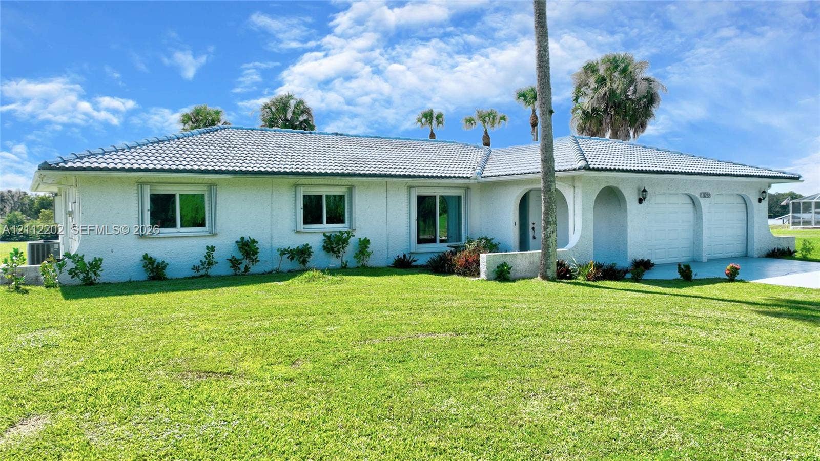 3233 Shell Lane, Labelle, FL 33935 Single-story exterior featuring white stucco siding, a grey tile roof, arched entryway, and an attached two-car garage