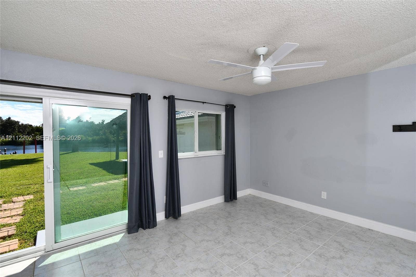 3233 Shell Lane, Labelle, FL 33935 Light-toned tile flooring, white ceiling fan, and sliding glass door with exterior access to a grass lawn and waterfront scenery