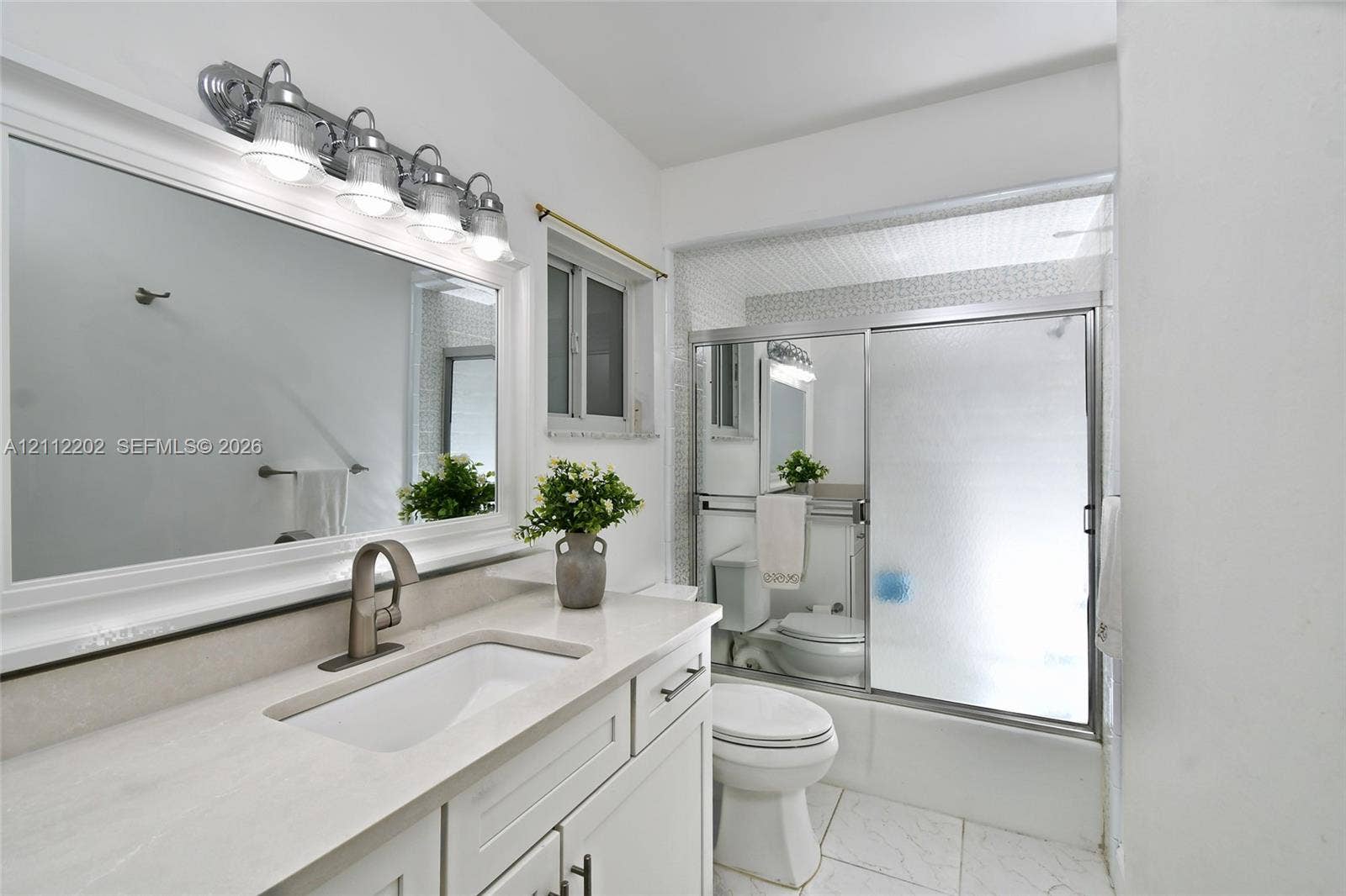 3233 Shell Lane, Labelle, FL 33935 Bathroom featuring a white vanity with a composite countertop, undermount sink, wide-frame mirror, four-light vanity fixture, and a shower-tub combination with sliding glass doors