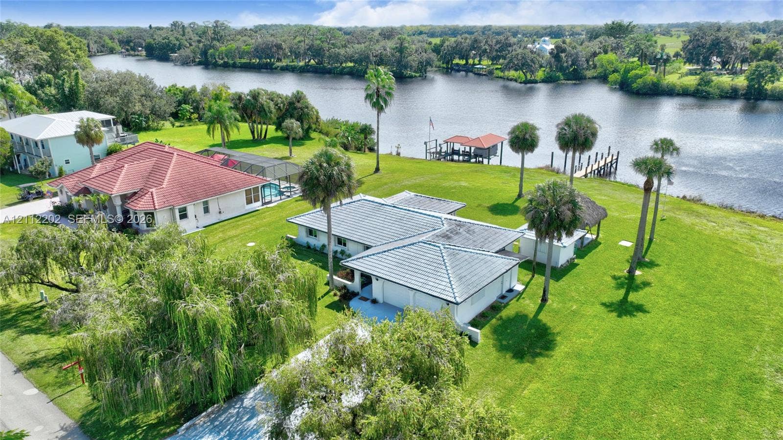 3233 Shell Lane, Labelle, FL 33935 Waterfront property featuring a private boat dock, sprawling lawn, mature palm trees, and a multi-car garage
