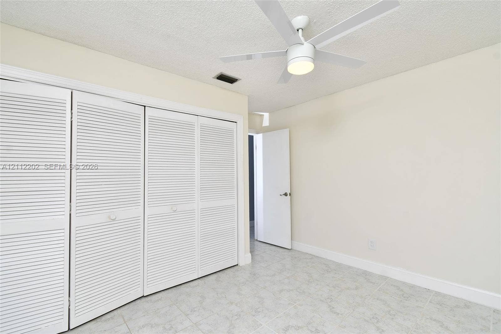 3233 Shell Lane, Labelle, FL 33935 Room featuring four-panel louvered closet doors, neutral wall finish, light-toned ceramic tile flooring, and a white ceiling fan with an integrated light fixture