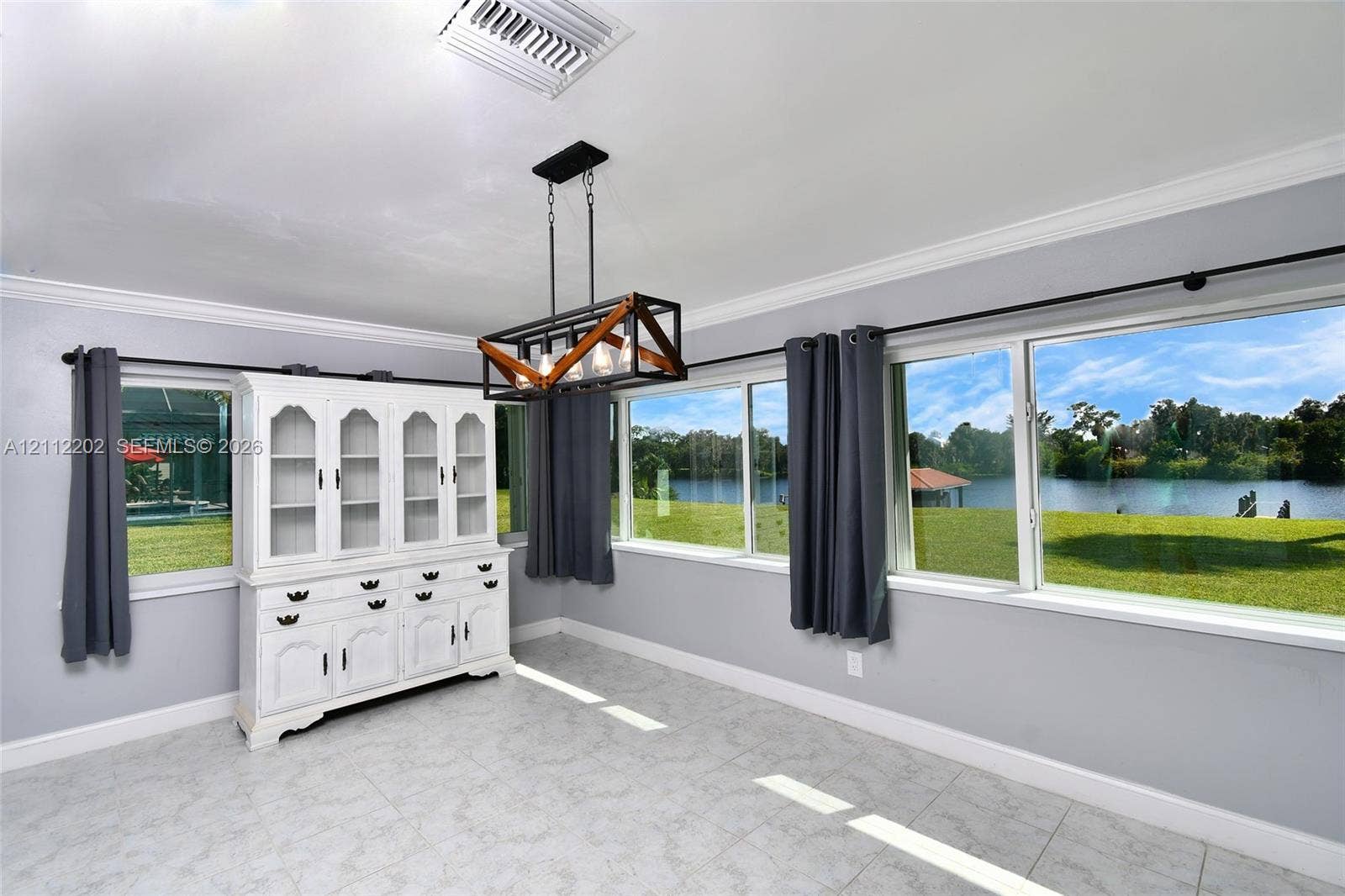 3233 Shell Lane, Labelle, FL 33935 Room featuring tile flooring, crown molding, a built-in white display cabinet, a linear geometric chandelier, and expansive windows offering a water backdrop