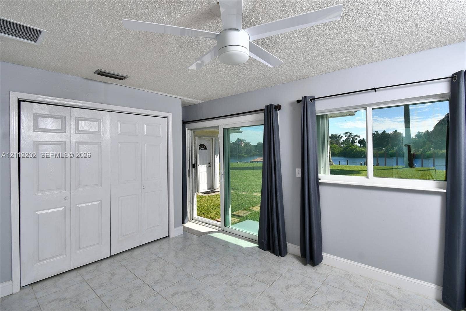 3233 Shell Lane, Labelle, FL 33935 Room interior featuring light-toned tile flooring, a multi-panel sliding glass door, a double-door reach-in closet, and a ceiling-mounted light fixture with fan blades