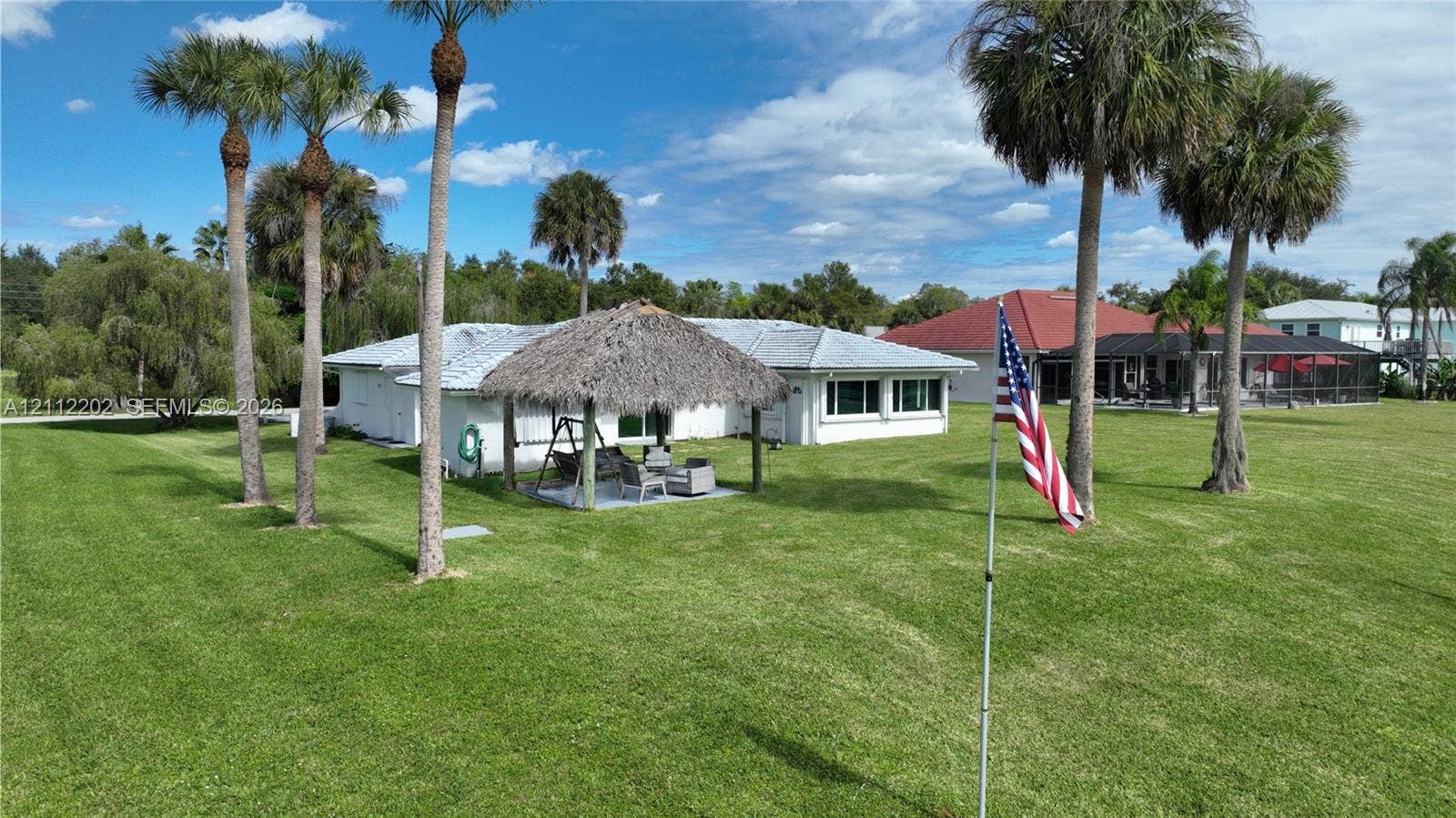 3233 Shell Lane, Labelle, FL 33935 Expansive manicured lawn featuring mature palm trees and a permanent tiki-style thatched-roof structure