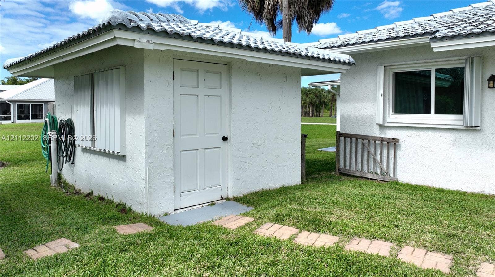 3233 Shell Lane, Labelle, FL 33935 Stucco exterior featuring a tiled roof, six-panel entry door, and a stone paver walkway set within a grass lawn