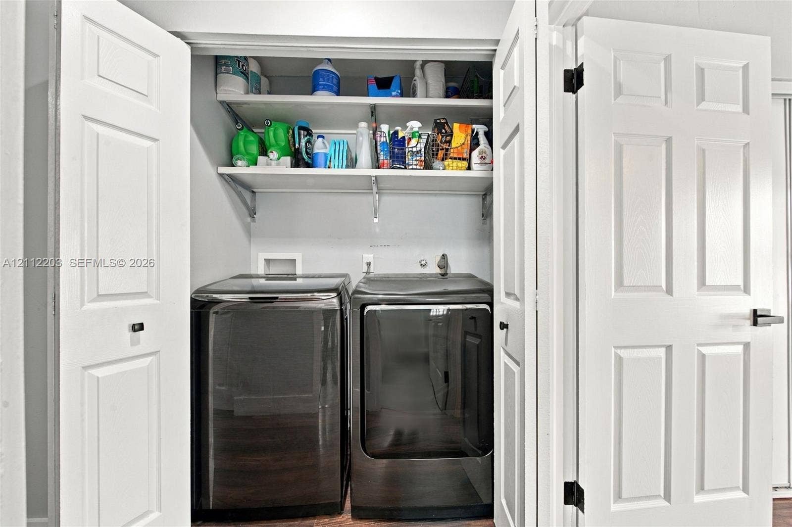 Laundry closet featuring white six-panel bi-fold doors and two tiered built-in storage shelves