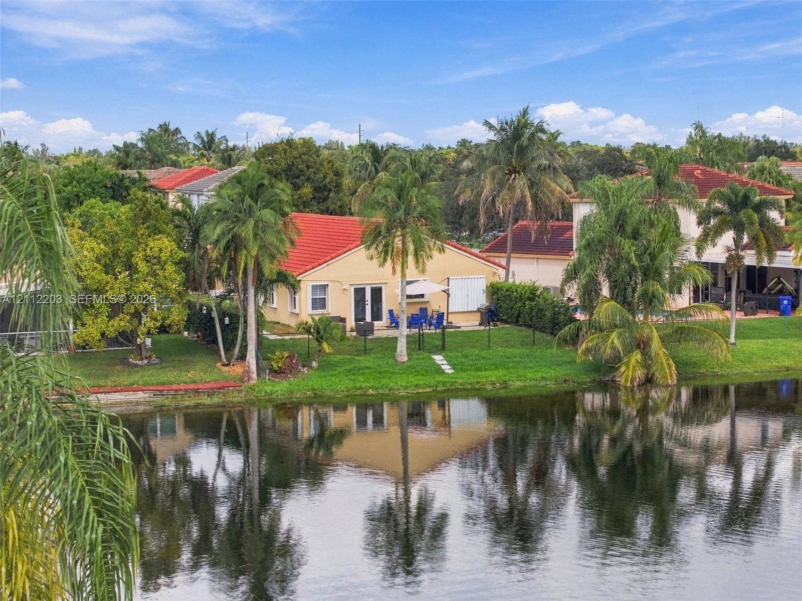 Waterfront residence featuring a tile roof, exterior stucco finish, lush landscaping with mature palms, and a manicured lawn