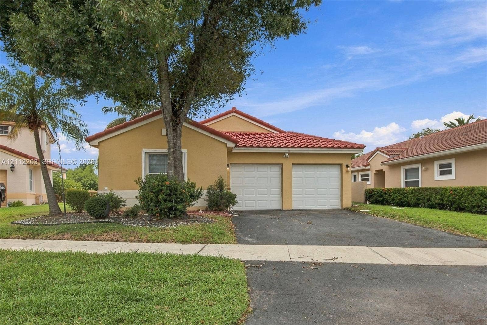 Stucco exterior featuring a dual-car garage, pitched tile roof, and mature landscaping