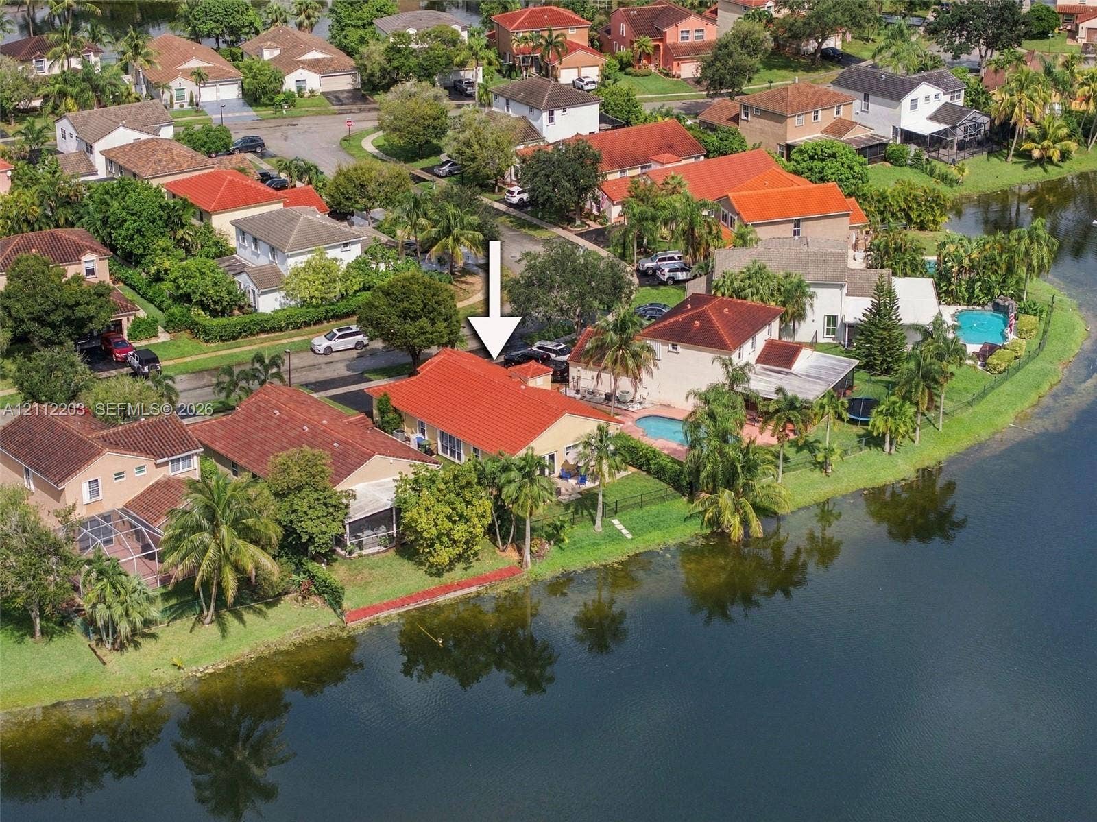 Waterfront property featuring a red tile roof, concrete driveway, and established tropical landscaping
