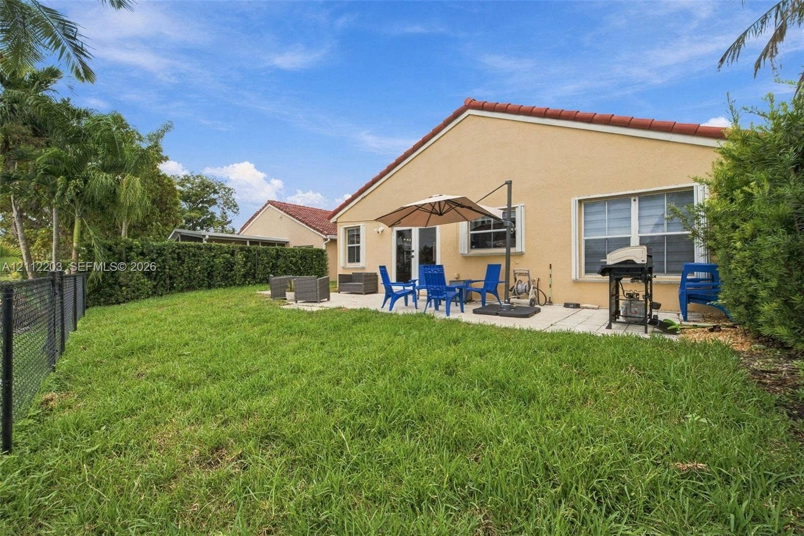 Backyard featuring a paved patio, perimeter chain-link fencing, mature privacy hedges, and a tile roof