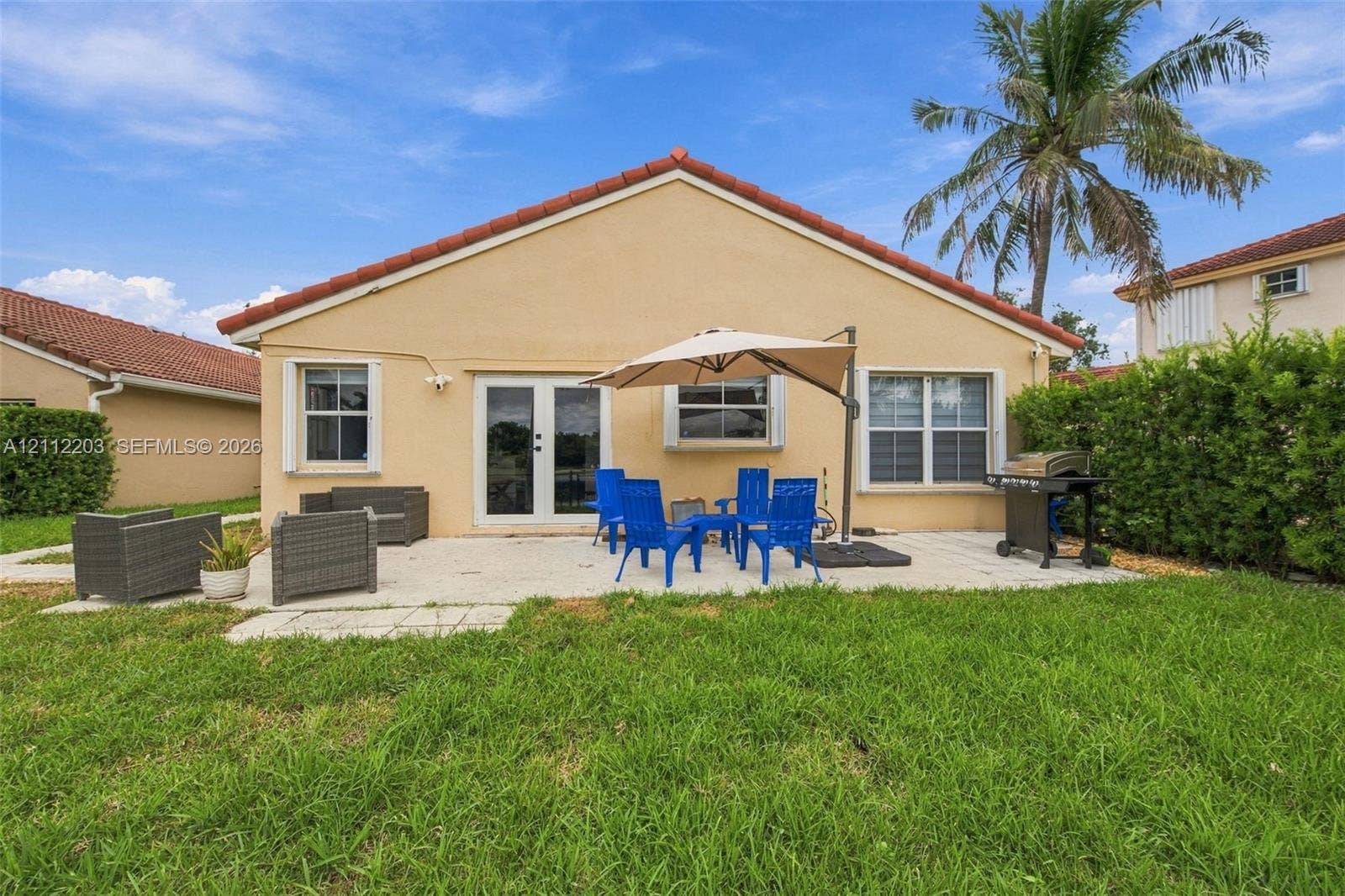 Rear exterior featuring a concrete patio, stucco siding, a tiled roof, and double glass doors