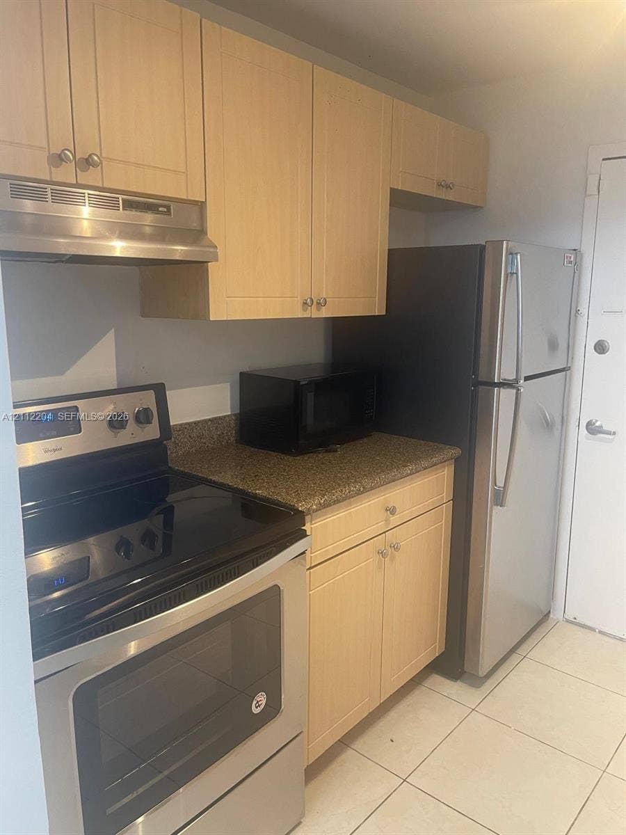 2020 NE 135th Street, #910, North Miami, North Miami, FL 33181 Kitchen featuring light wood-finish cabinetry, stone-texture countertop, stainless steel range with overhead hood, and ceramic tile flooring