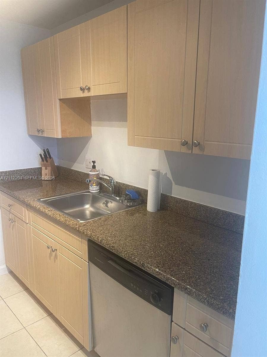 2020 NE 135th Street, #910, North Miami, North Miami, FL 33181 Light-toned cabinetry, speckled stone-finish countertops, stainless steel sink with metal faucet, integrated dishwasher, and ceramic tile flooring