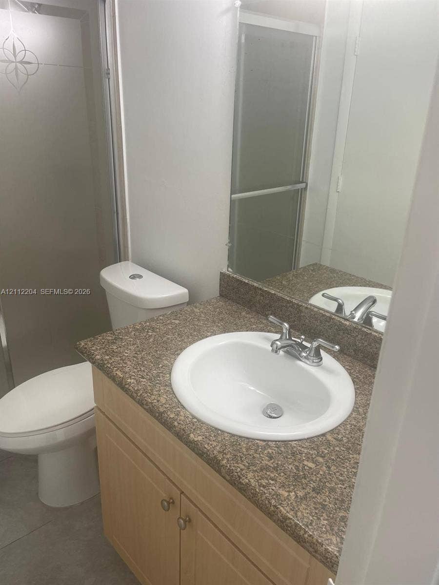 2020 NE 135th Street, #910, North Miami, North Miami, FL 33181 Bathroom vanity featuring a light wood-finish cabinet, stone-composite countertop, integrated porcelain sink, and a walk-in shower with a frosted glass door