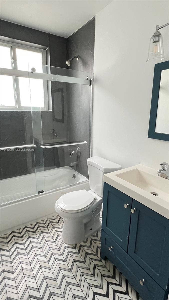 1115 Euclid Avenue, #5, Miami Beach, Miami Beach, FL 33139 Bathroom featuring herringbone-patterned tile flooring, a blue-finished vanity cabinet with an integrated sink, a glass-enclosed shower, and dark-toned wall tile surround
