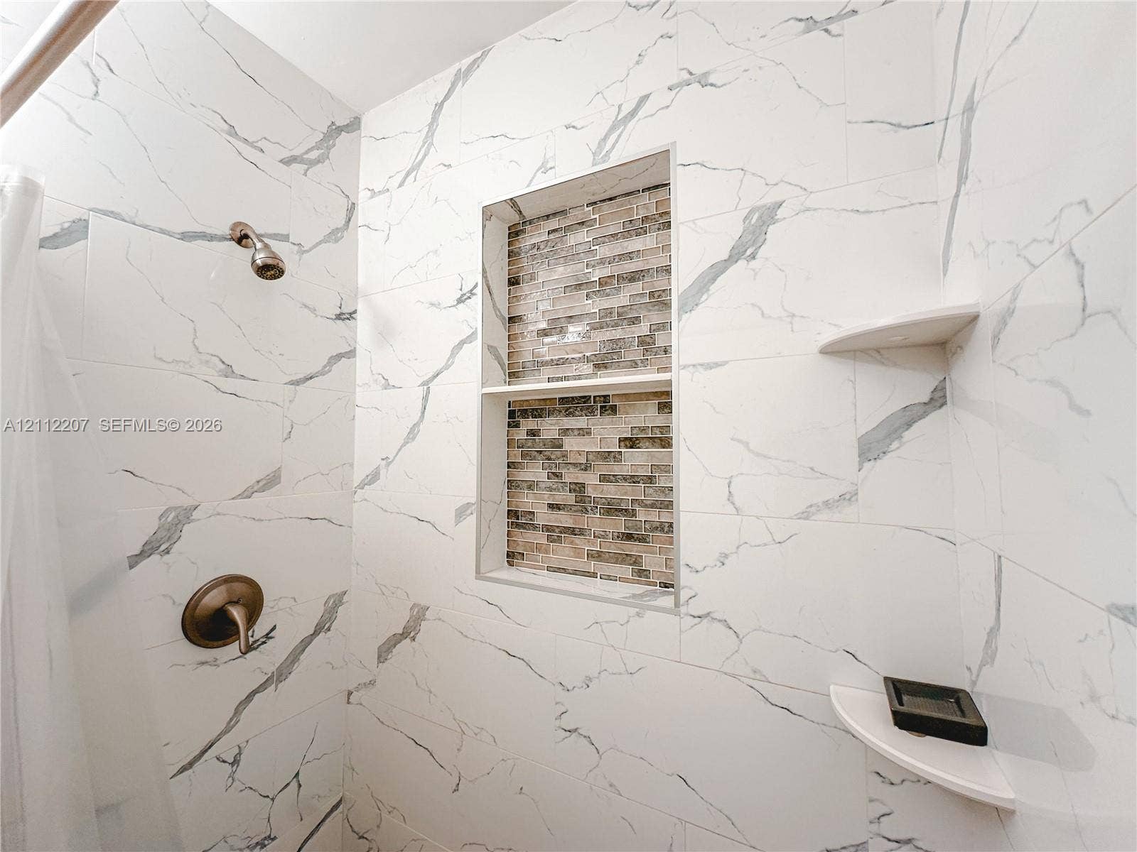 525 SW 67th Avenue, Miami, Miami, FL 33144 Shower surround finished with large-format white veined tile, a multi-tier built-in tiled niche with decorative mosaic detailing, two integrated corner shelves, and a metal finish wall-mounted shower fixture