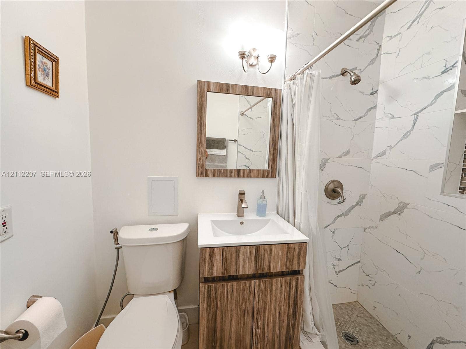 525 SW 67th Avenue, Miami, Miami, FL 33144 Bathroom featuring a wood-finish vanity with a rectangular sink, wall-mounted metallic lighting fixture, and shower enclosure with floor-to-ceiling stone-patterned wall tile