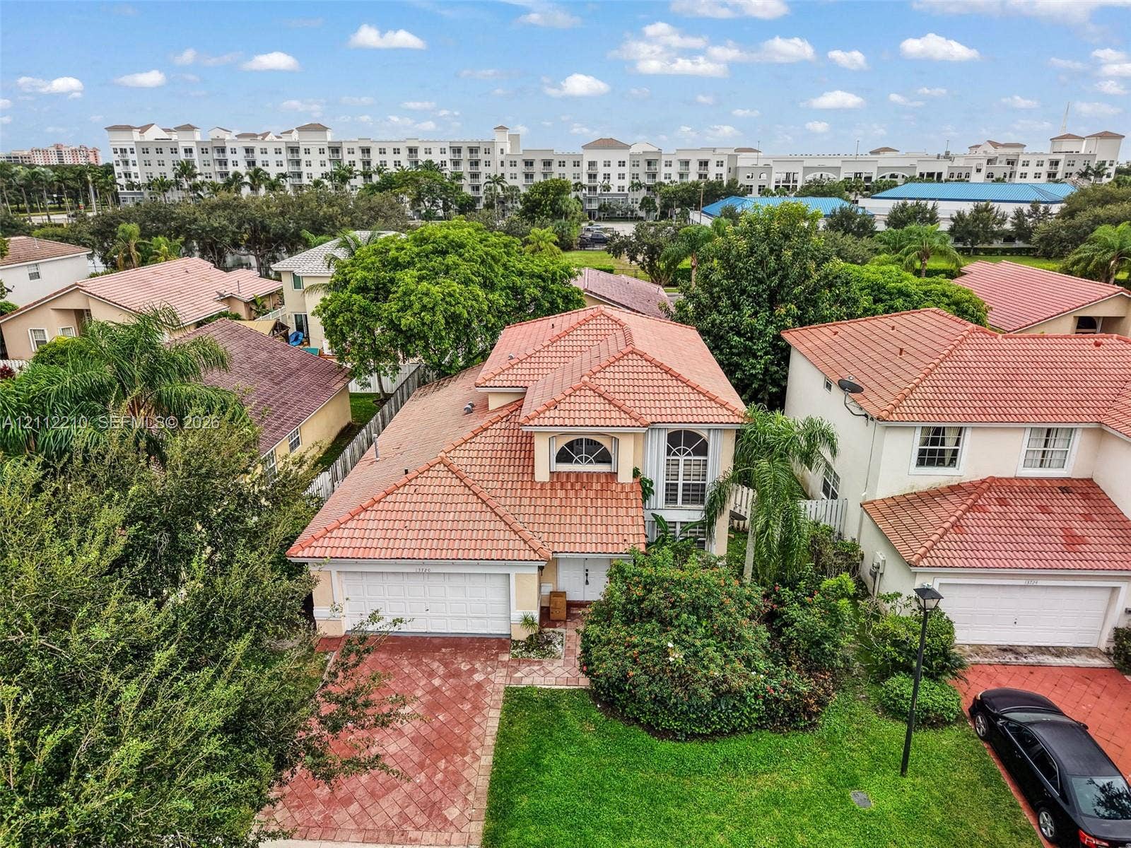 Two-story residence featuring a terracotta-tiled roof, arched architectural windows, a multi-car garage, and patterned paver driveway
