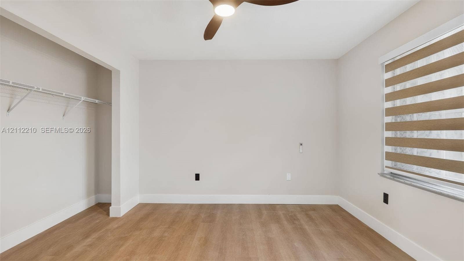 Room featuring wood-finish flooring, a ceiling fan with integrated lighting, a built-in wire closet shelving system, and window treatments
