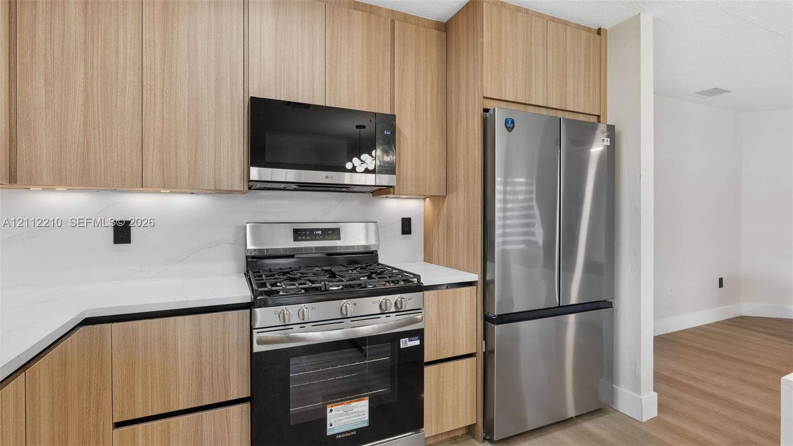 Kitchen featuring flat-panel wood-finish cabinetry, white solid-surface countertops, stainless steel appliances, and integrated under-cabinet lighting