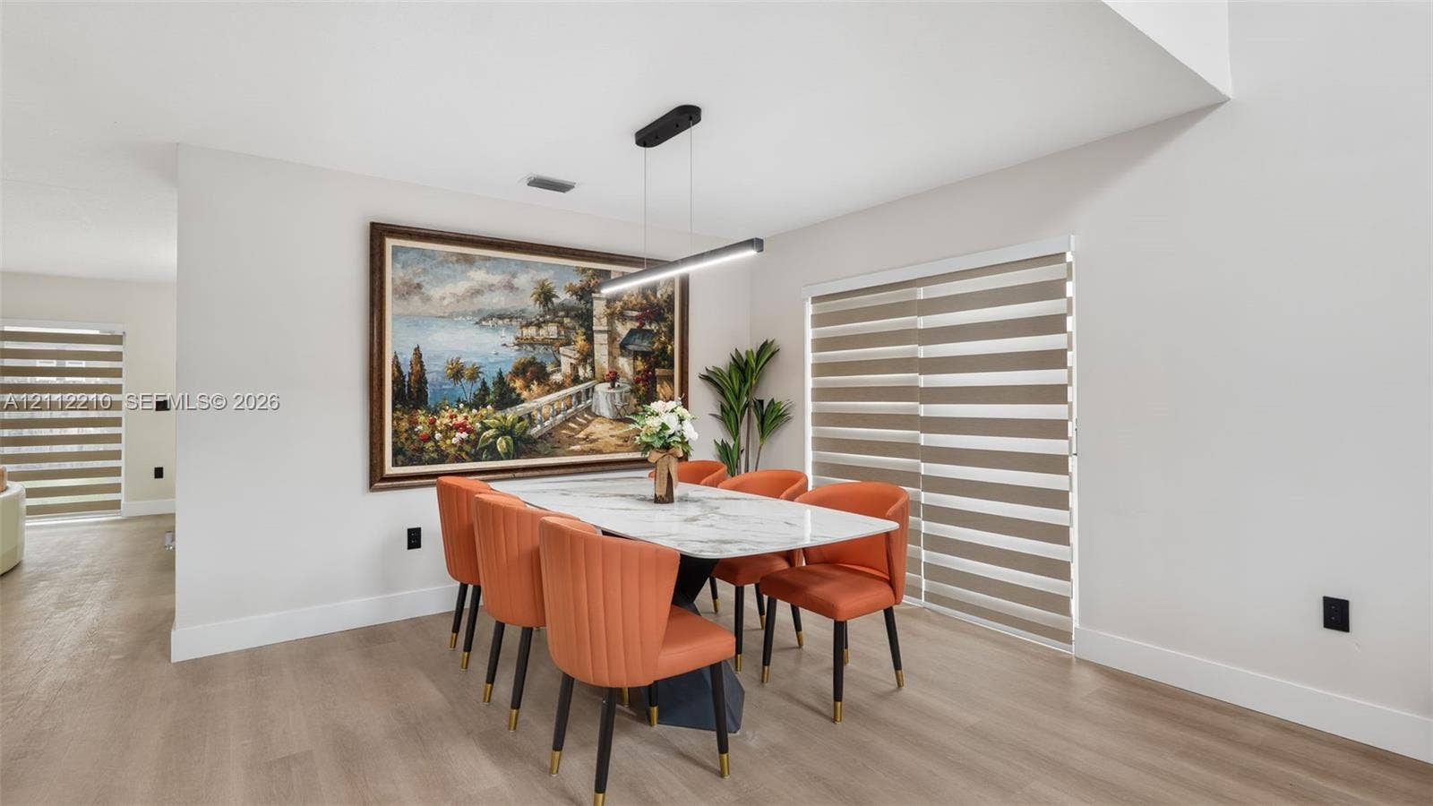 Dining area featuring wood-finish flooring, modern linear pendant lighting, and dual sliding glass doors with adjustable roller shades