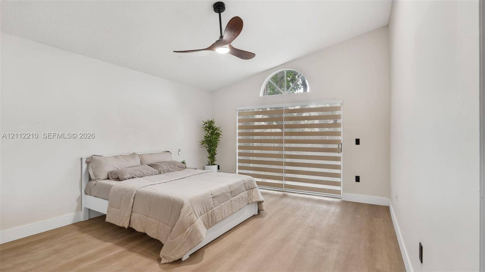 Vaulted ceiling featuring a three-blade ceiling fan, wood-finish flooring, and a sliding glass door topped with a semicircular window