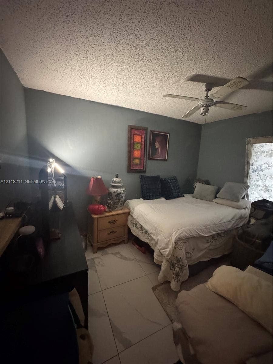 Large-format tile flooring, textured ceiling finish, and ceiling-mounted fan with integrated light fixture