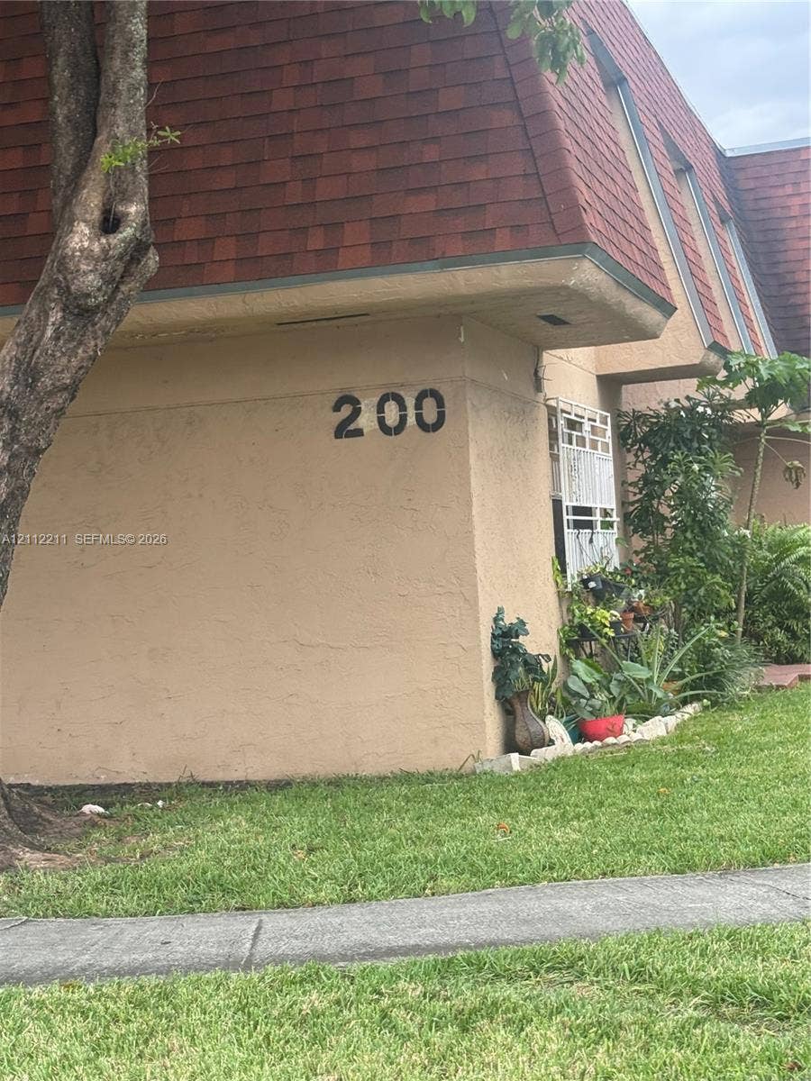 Exterior facade featuring textured stucco finish, dark red asphalt shingle mansard roof, and metal window security grate