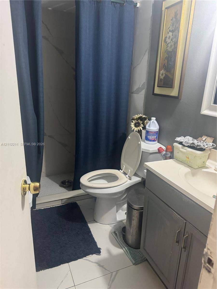 Bathroom featuring a vanity with a white countertop, large-format tile flooring, and a walk-in shower with stone-patterned wall tiling