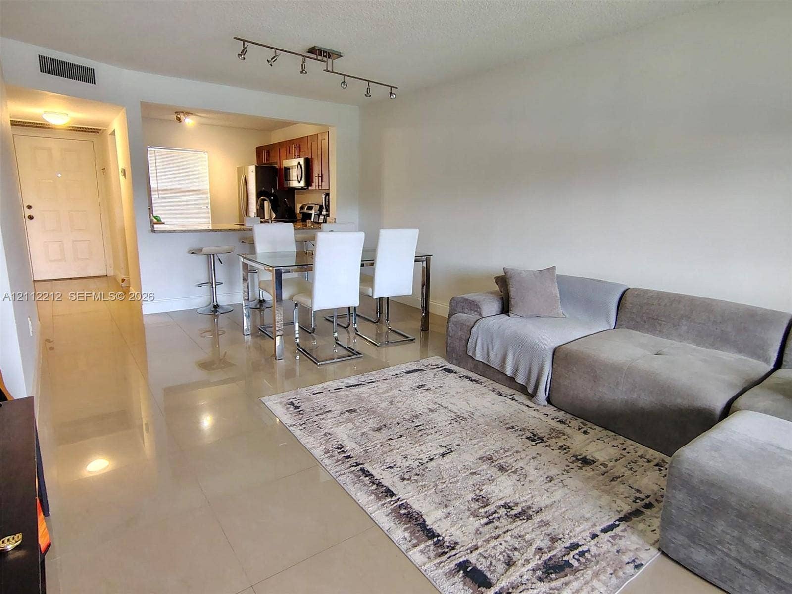 2900 NW 42nd Avenue, #304A, Coconut Creek, Coconut Creek, FL 33066 Open-concept interior featuring large-format tile flooring, recessed track lighting, and a kitchen pass-through window with a stone-surfaced breakfast bar