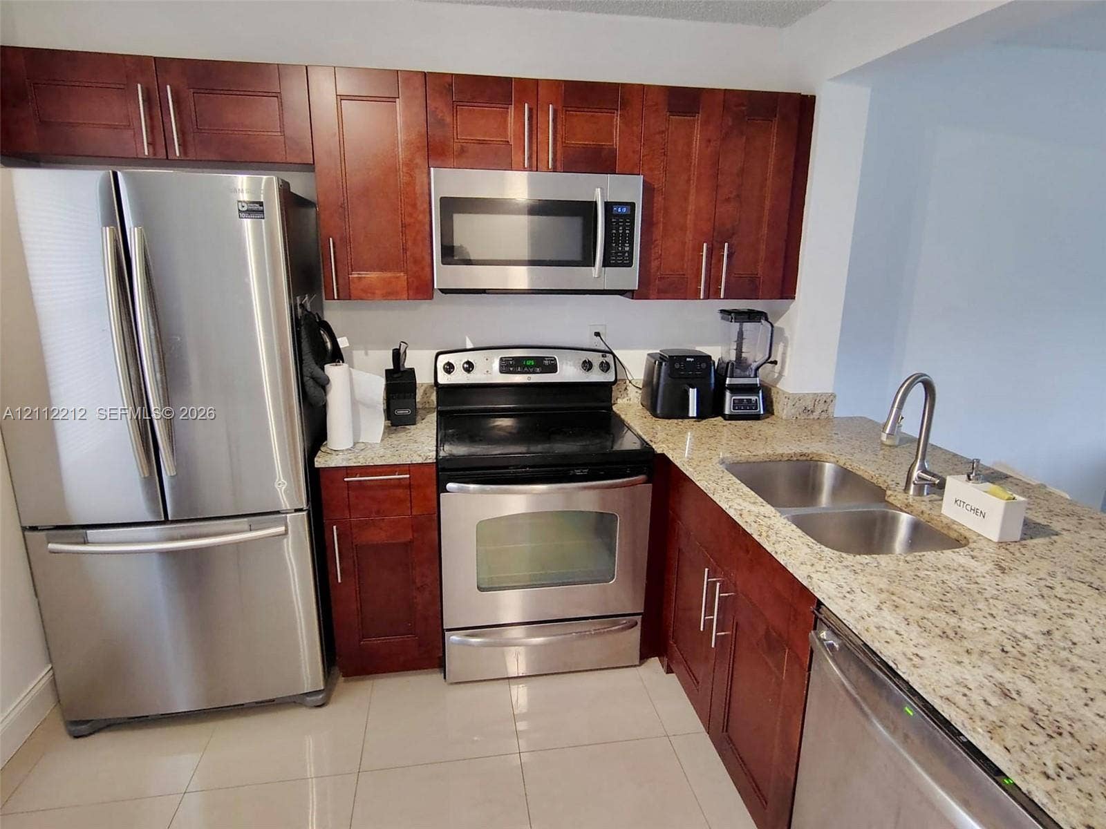 2900 NW 42nd Avenue, #304A, Coconut Creek, Coconut Creek, FL 33066 Kitchen featuring cherry-tone cabinetry, stone-finish countertops, stainless steel appliances, a dual-basin undermount sink, and light-tone tile flooring