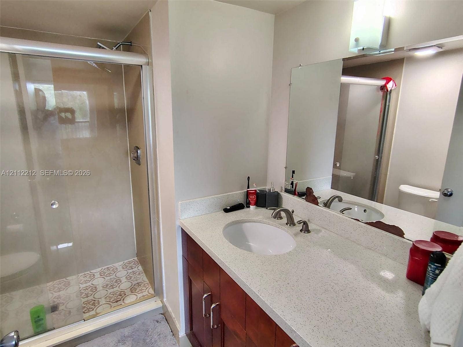 2900 NW 42nd Avenue, #304A, Coconut Creek, Coconut Creek, FL 33066 Bathroom featuring a vanity with wood-finish cabinetry, quartz countertop, and undermount sink, complemented by a glass-enclosed shower with patterned tile flooring and a wall-mounted mirror