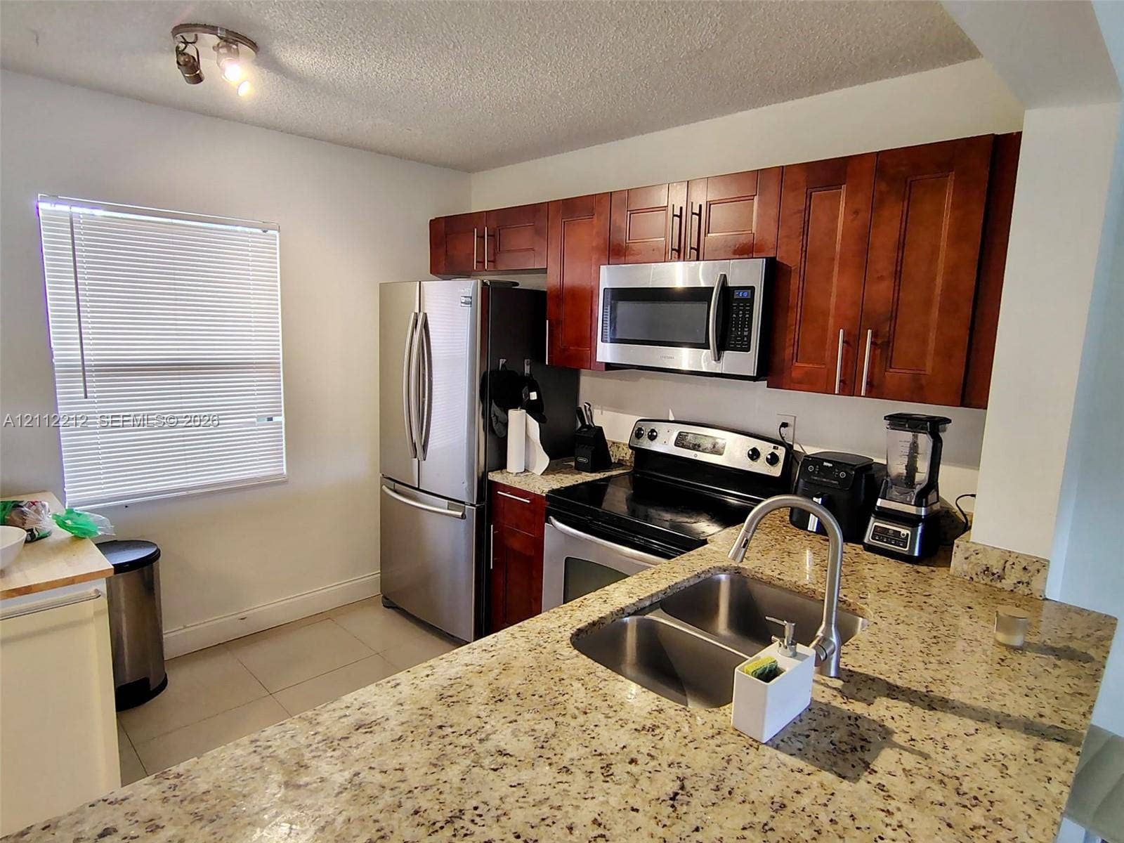2900 NW 42nd Avenue, #304A, Coconut Creek, Coconut Creek, FL 33066 Kitchen featuring cherry-finish cabinetry, stone countertops, stainless steel appliances, and a dual-basin undermount sink with a high-arch faucet
