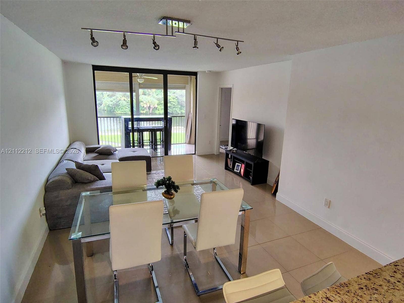2900 NW 42nd Avenue, #304A, Coconut Creek, Coconut Creek, FL 33066 Open-concept floor plan with large-format tile flooring, multi-directional ceiling track lighting, and full-height sliding glass doors leading to a screened balcony