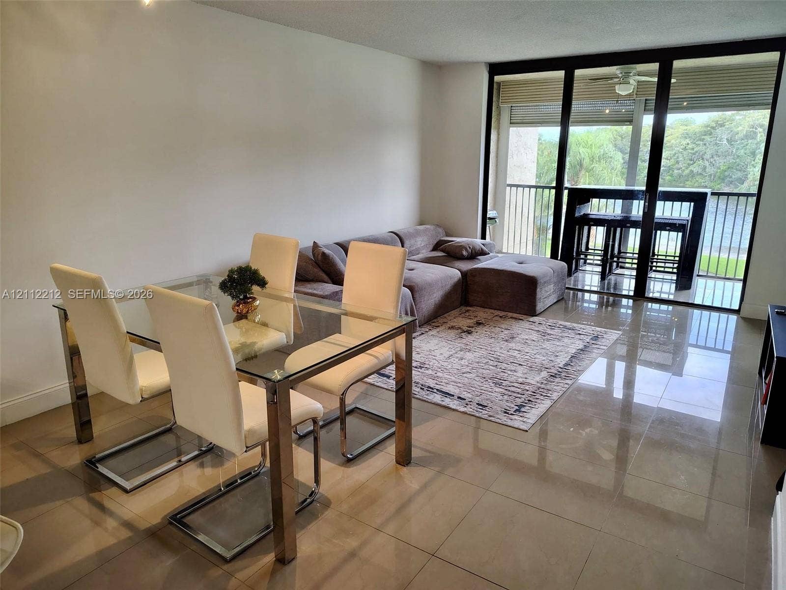 2900 NW 42nd Avenue, #304A, Coconut Creek, Coconut Creek, FL 33066 Living area featuring large-format tile flooring, floor-to-ceiling glass sliding doors, and a screened balcony with metal railing