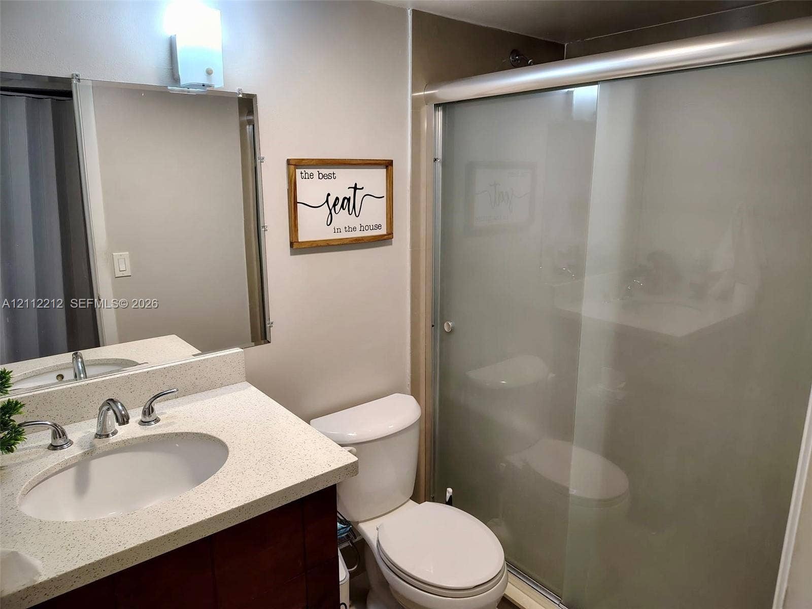 2900 NW 42nd Avenue, #304A, Coconut Creek, Coconut Creek, FL 33066 Bathroom featuring a vanity with a light-toned solid surface countertop, an undermount sink with dual-handle metal faucet, a rectangular wall-mounted mirror, and a walk-in shower with frosted sliding glass doors