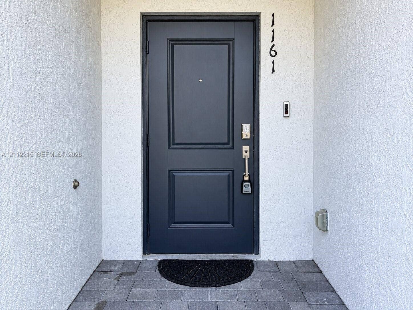 1161 SE 1 Street, #0, Florida City, Florida City, FL 33034 Dark-toned paneled entry door with a metallic peephole, matte-finish hardware, and exterior stone pavers