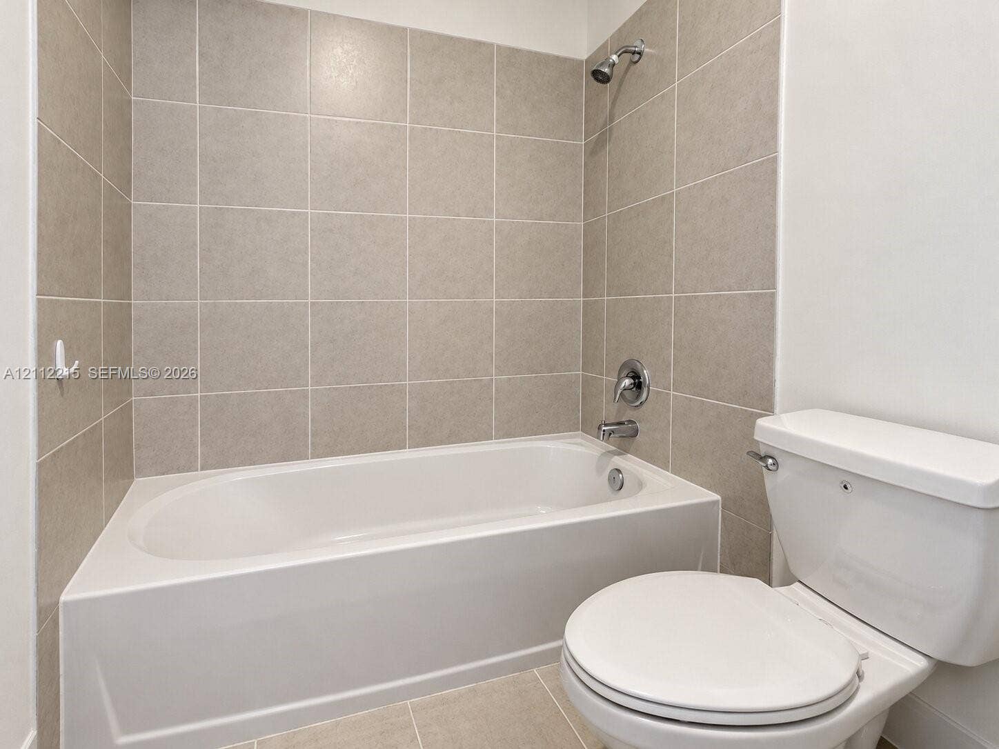 1161 SE 1 Street, #0, Florida City, Florida City, FL 33034 Bathroom featuring a composite soaking tub, a wall-mounted shower head with integrated diverter, neutral-toned square tile tub surround, and a porcelain commode