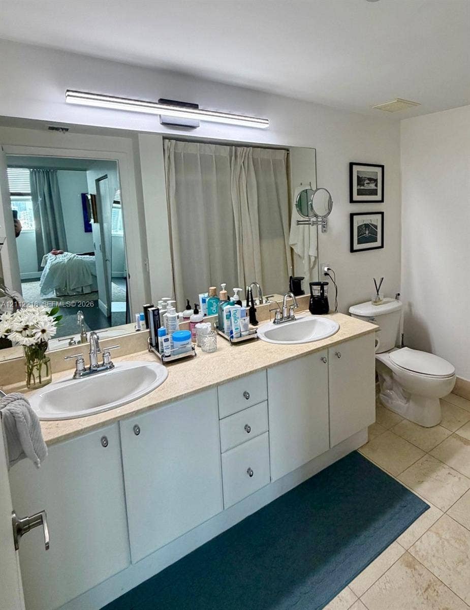 2475 Brickell Avenue, #1905, Miami, Miami, FL 33129 Dual-sink vanity with a solid-surface countertop, integrated oval basins, chrome-finish dual-handle faucets, and a full-width wall mirror with integrated LED light fixture