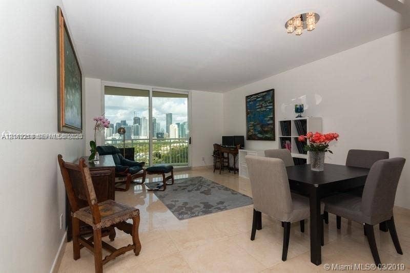 2475 Brickell Avenue, #1905, Miami, Miami, FL 33129 Open-concept interior featuring light-toned tile flooring, floor-to-ceiling sliding glass doors, a metal-railed balcony, and a multi-bulb flush-mount ceiling fixture
