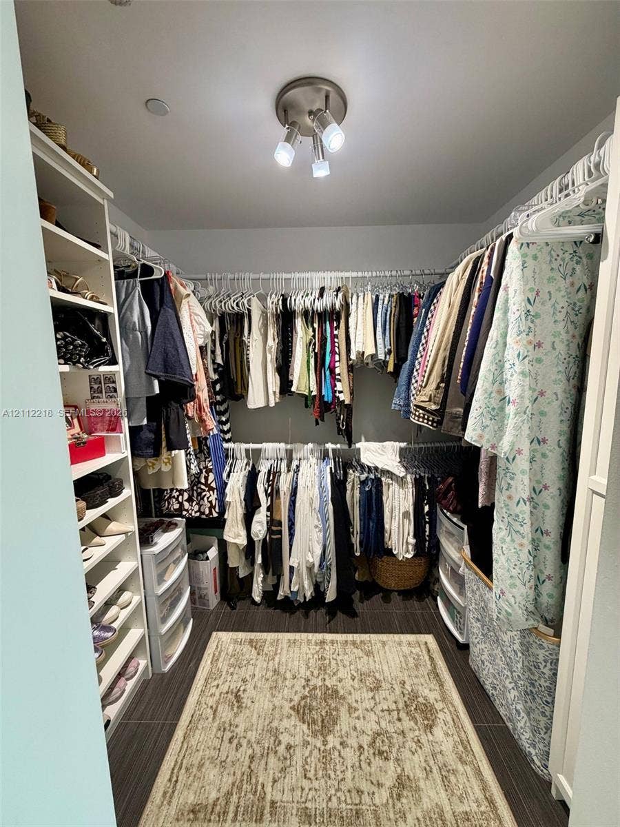 2475 Brickell Avenue, #1905, Miami, Miami, FL 33129 Walk-in closet featuring built-in vertical shelving, tiered hanging rods, and dark tile flooring with a brushed-nickel triple-light fixture