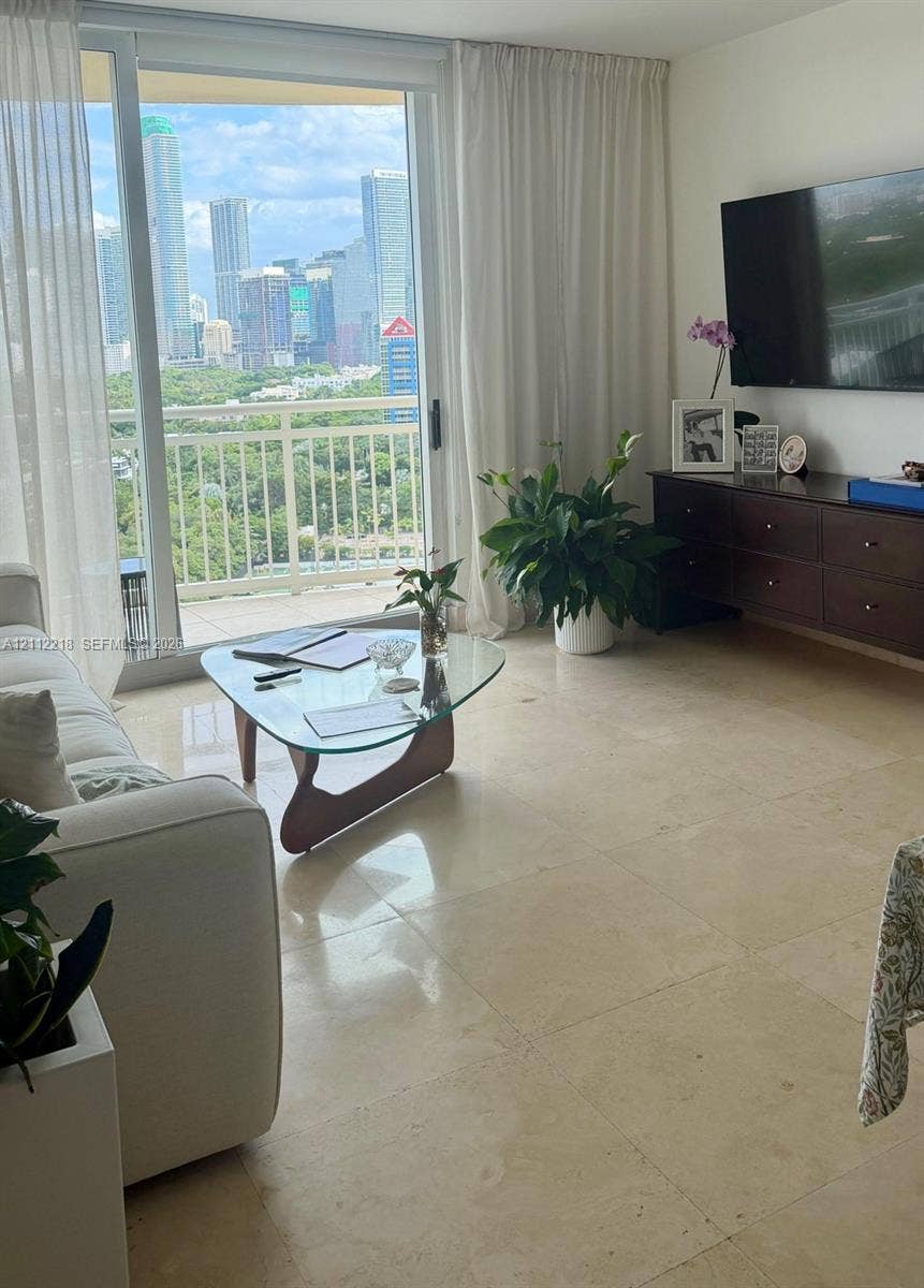 2475 Brickell Avenue, #1905, Miami, Miami, FL 33129 Floor-to-ceiling sliding glass doors opening to a balcony with metal railings and expansive city skyline scenery, complemented by large-format light-toned stone flooring