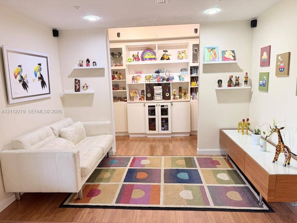 Built-in floor-to-ceiling cabinetry with glass-panel doors, recessed ceiling lighting, wood-finish flooring, and wall-mounted floating shelves