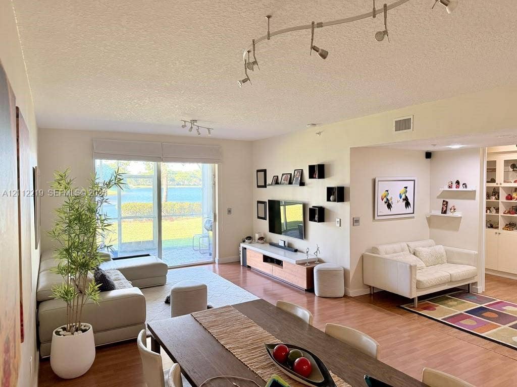Living area featuring wood-finish flooring, adjustable track lighting, and sliding glass doors with screen enclosure