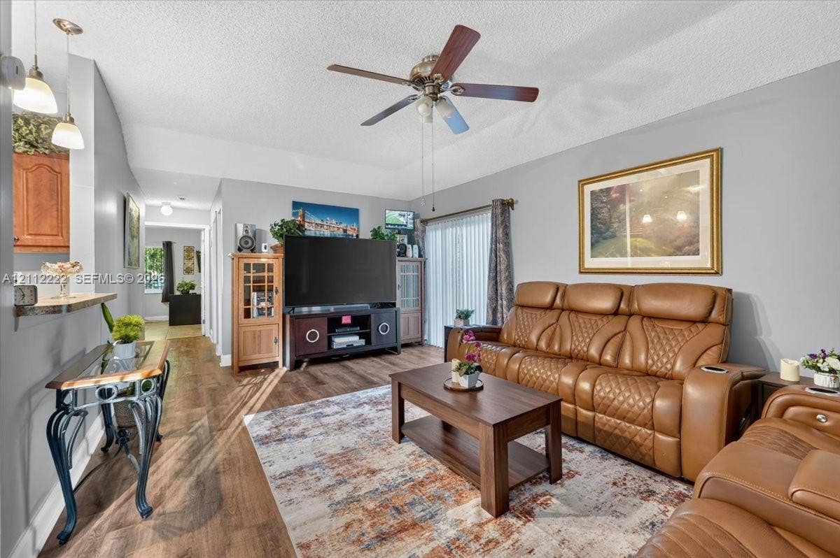 Living area featuring wood-finish flooring, vaulted ceilings, a ceiling fan, and sliding glass doors
